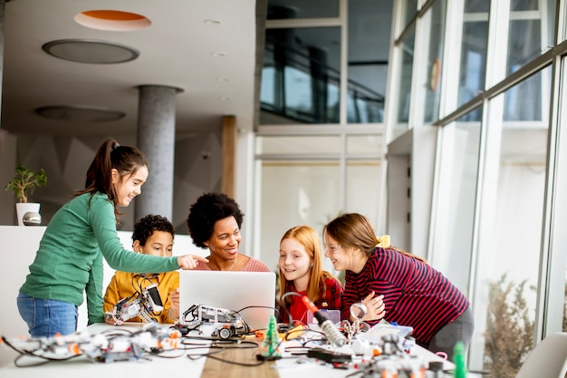 Grupo de niños felices con su profesora de ciencias afroamericana con programación de portátiles juguetes eléctricos y robots en el aula de robótica
