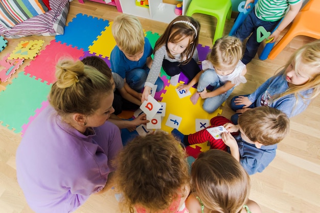 Foto grupo de niños de jardín de infantes sentados en el piso junto con un maestro que brinda trabajo en grupo niños aprendiendo a cooperar mientras resuelven tareas