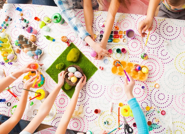 Grupo de niños y madres pintando huevos de Pascua. vista superior de la mesa y las manos de los creadores juntos