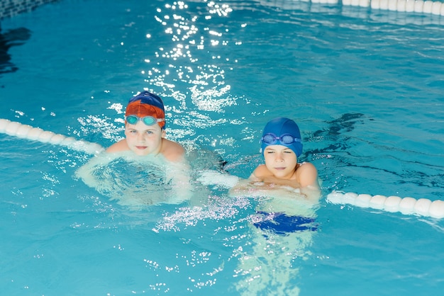 Un grupo de niños y niñas se entrenan y aprenden a nadar en la piscina con un monitor. Desarrollo del deporte infantil.