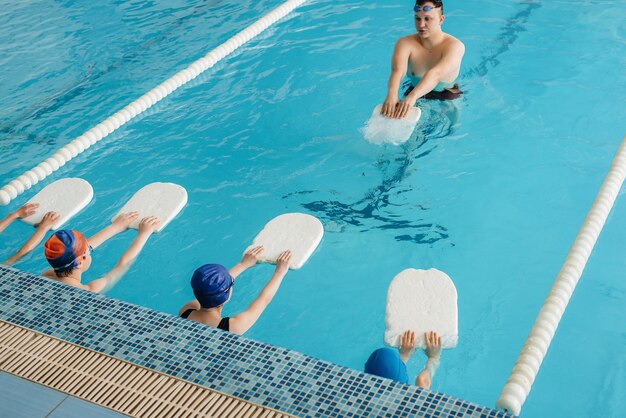 Un grupo de niños y niñas se entrenan y aprenden a nadar en la piscina con un monitor. Desarrollo del deporte infantil.