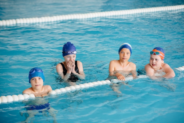 Un grupo de niños y niñas se entrenan y aprenden a nadar en la piscina con un monitor. Desarrollo del deporte infantil.