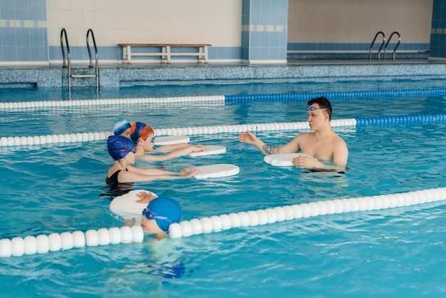 Un grupo de niños y niñas se entrenan y aprenden a nadar en la piscina con un monitor. Desarrollo del deporte infantil.