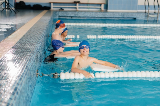 Un grupo de niños y niñas se entrenan y aprenden a nadar en la piscina con un monitor. Desarrollo del deporte infantil.