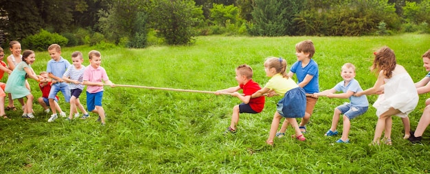 El grupo de niños y niñas jugando tira y afloja en el césped en verano