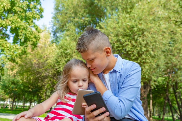 Grupo de niños ocupados mirando sus teléfonos enviando mensajes de texto y jugando sentados afuera