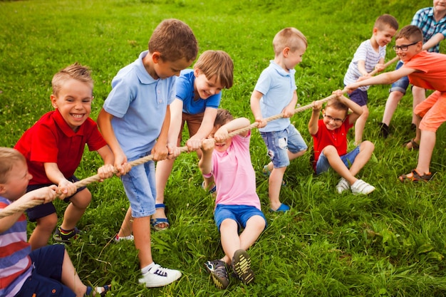 El grupo de niños pequeños felices está jugando tira y afloja afuera en la hierba