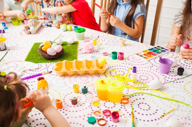 Grupo de niños pintando huevos en la mesa. Amigos felices preparándose para la Pascua.