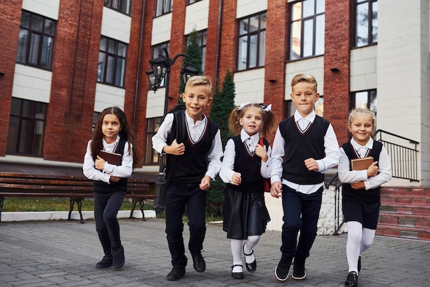 Grupo de niños en uniforme escolar posando para la cámara al aire libre junto al edificio de educación.