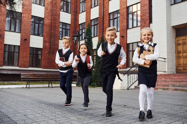 Grupo de niños en uniforme escolar posando para la cámara al aire libre junto al edificio de educación.