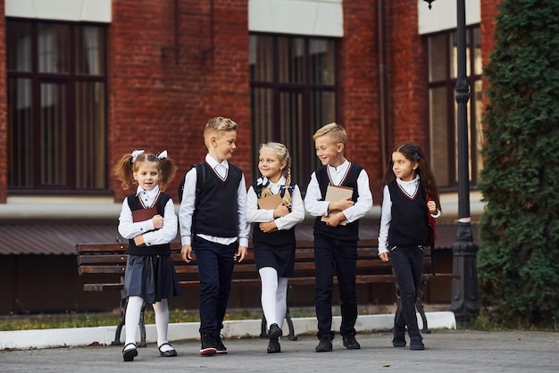 Grupo de niños en uniforme escolar que está al aire libre junto al edificio de educación.