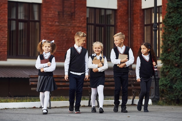 Grupo de niños en uniforme escolar que está al aire libre junto al edificio de educación.