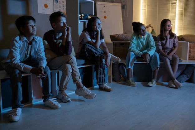 Grupo de niños viendo una película o algo más en la oscuridad.