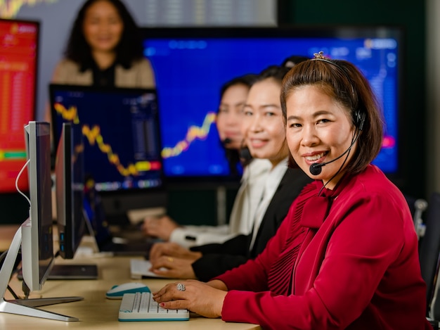 Grupo de operadores de servicio al cliente de mujeres asiáticas lleva auriculares con micrófono sentarse sonriendo gráfico frontal