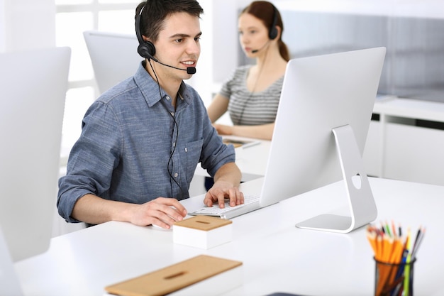 Foto grupo de operadores en el trabajo centro de llamadas enfoque en recepcionista de hombre en auriculares en servicio al cliente