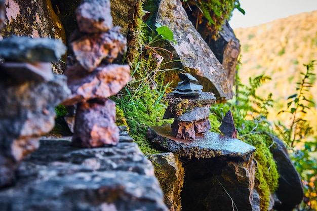 Grupo de pequeñas rocas cairn apiladas contra la pared de piedra con musgo y rocas cubiertas de líquenes