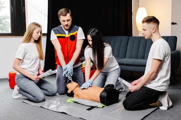 Grupo de personas aprendiendo a hacer compresiones cardíacas de primeros auxilios con maniquíes durante el entrenamiento en interiores