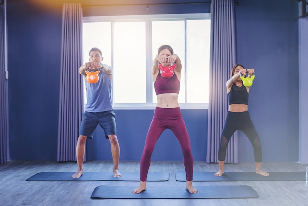 Grupo de personas aptas que sostienen la campana de la caldera durante una clase de ejercicios en el gimnasio.