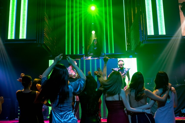 Grupo de personas bailan en la discoteca al ritmo de la música de DJ en el escenario