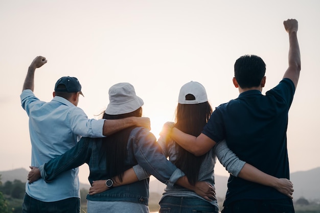 Grupo de personas con los brazos levantados mirando el amanecer en el fondo de la montaña