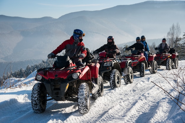 Grupo de personas conduciendo quads fuera de carretera en la nieve en la cima de la montaña en invierno