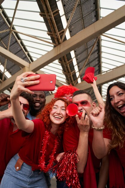 Grupo de personas de diferentes razas animando a su equipo y tomando un selfie en el estadio de fútbol