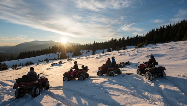 Grupo de personas disfrutando del atardecer en quads en la nieve en las montañas en invierno