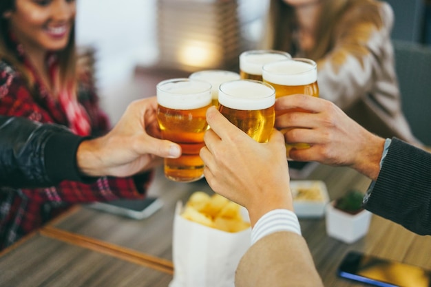 Grupo de personas divirtiéndose animando con cerveza dentro del bar de la cervecería Enfoque en la mano delantera sosteniendo el vidrio