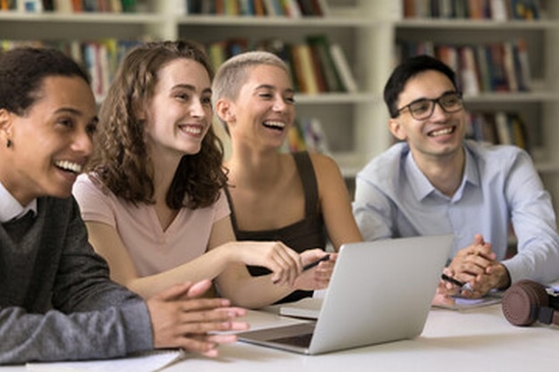 un grupo de personas están sentadas alrededor de una computadora portátil y sonriendo