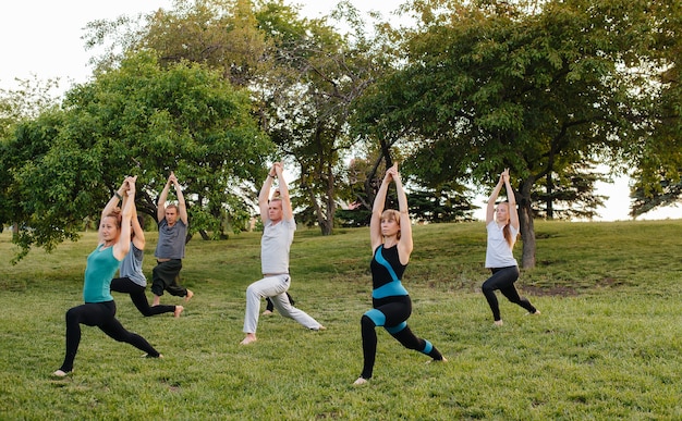 Un grupo de personas hacen yoga en el parque al atardecer.