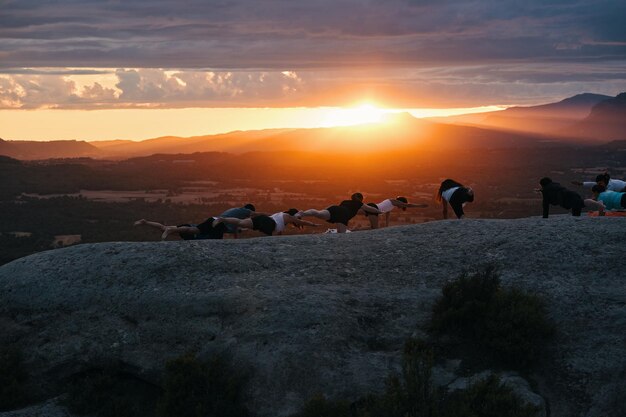 Un grupo de personas haciendo yoga en una colina con la puesta de sol detrás de ellos