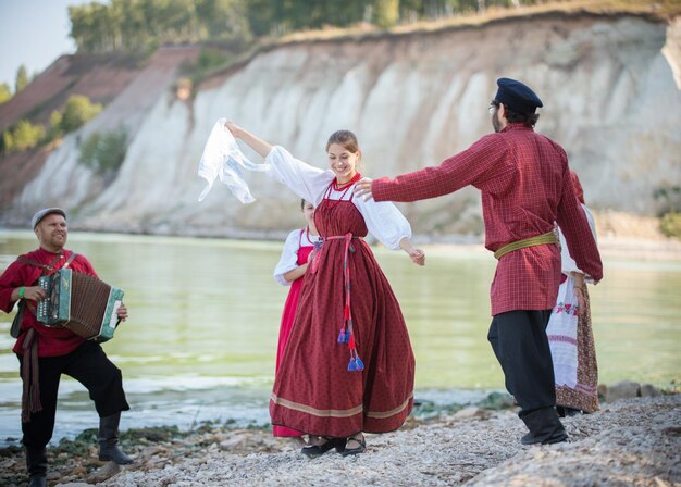 Un grupo de personas con hermosas ropas folclóricas rusas bailando contra el agua, bailando en el centro de una niña, de cerca
