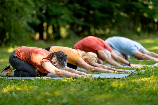 Grupo de personas maduras practicando yoga juntos al aire libre haciendo poses para niños