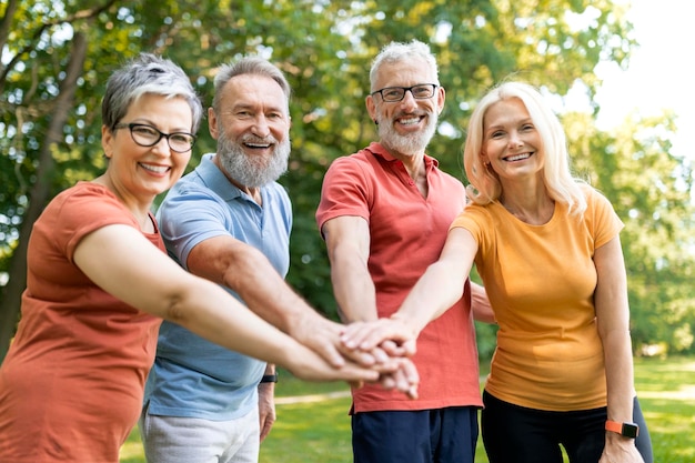 Grupo de personas mayores alegres apilando las manos después de hacer ejercicio deportivo al aire libre