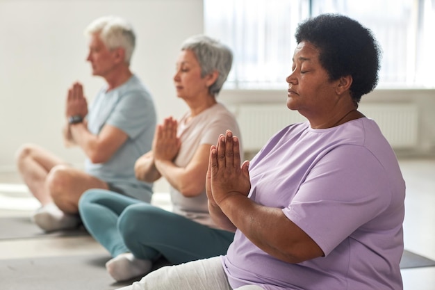 Grupo de personas mayores meditando en posición de loto en clase de yoga