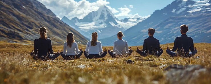 un grupo de personas meditando frente a una montaña con montañas en el fondo