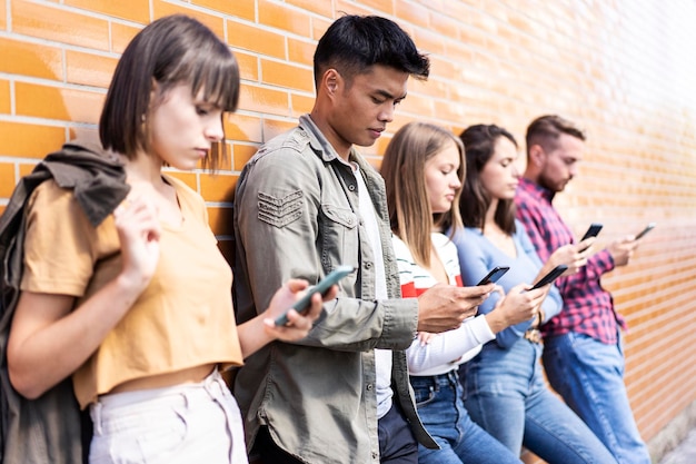 Grupo de personas multiculturales que usan teléfonos inteligentes en el patio trasero de la universidad Amigos milenarios adictos al teléfono inteligente móvil Concepto de tecnología con estudiantes siempre conectados Filtro vívido cálido