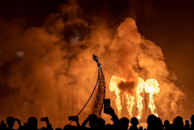Grupo de personas observando a una persona volando contra una exhibición de fuegos artificiales por la noche