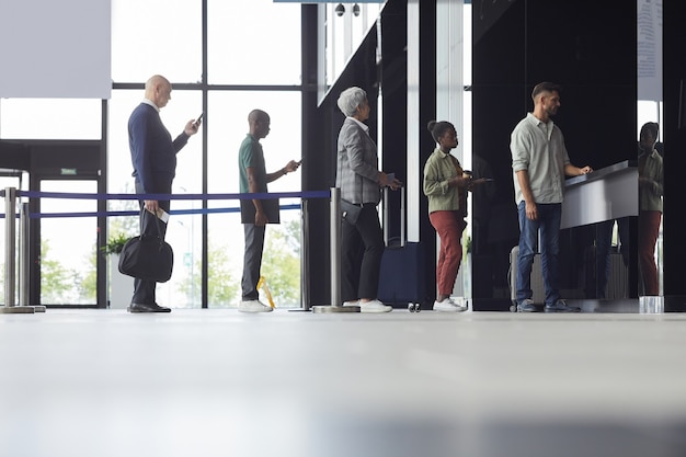 Grupo de personas de pie en una fila y comprando boletos para el avión en el aeropuerto.