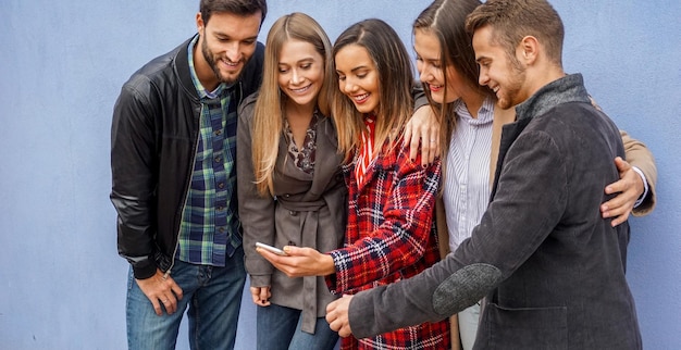 Grupo de personas de pie junto a la pared y compartiendo cosas en línea Amigos revisando sus teléfonos inteligentes Concepto de tecnología