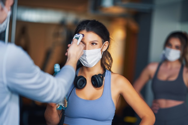 Grupo de personas que usan máscaras y se les mide la temperatura antes de ingresar al gimnasio.