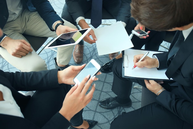 Grupo de personas que usan teléfonos inteligentes sentados en la reunión, cerca de las manos.