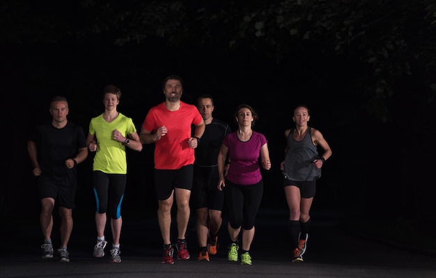 Grupo de personas sanas corriendo en el parque de la ciudad, equipo de corredores en entrenamiento nocturno