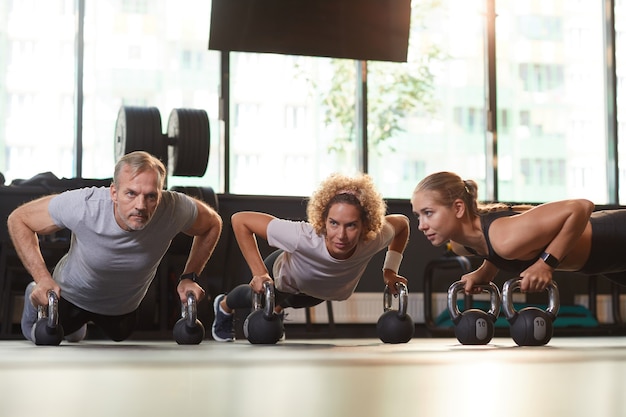 Grupo de personas sanas entrenando con pesas en el piso que hacen ejercicios físicos durante el entrenamiento en el gimnasio