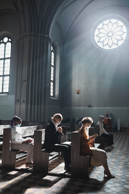 Grupo de personas sentadas en un banco en la hermosa iglesia antigua orando juntos durante una misa