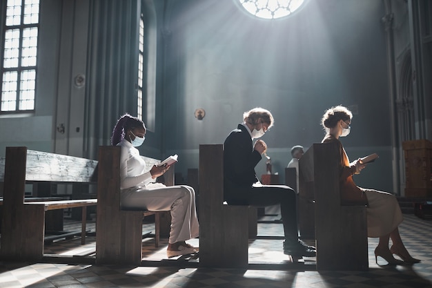 Grupo de personas sentadas en el banco y rezando en la hermosa iglesia antigua