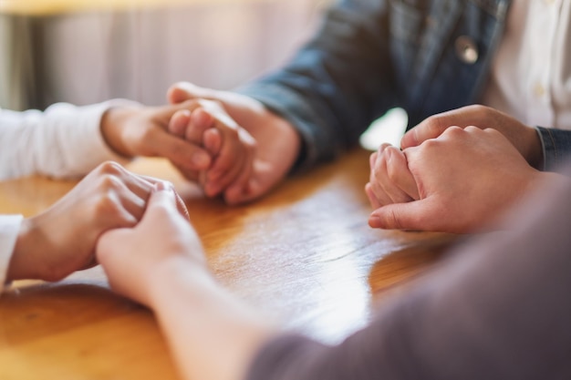 Grupo de personas sentadas en un círculo tomados de la mano y rezar juntos o en sesión de terapia