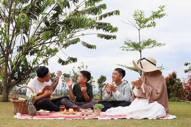 Un grupo de personas se sientan en una manta frente a un árbol y disfrutan de un picnic.