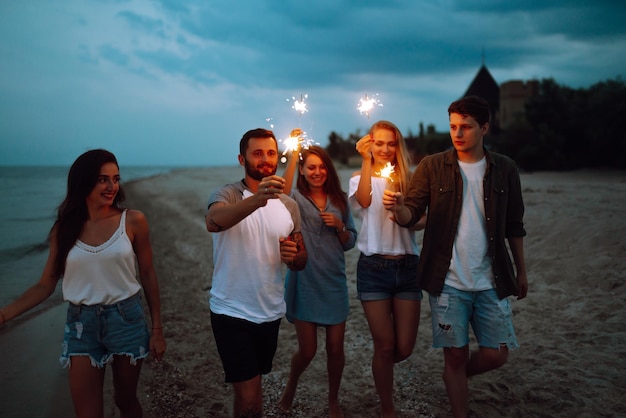 Grupo de personas sosteniendo bengalas en la fiesta en la playa Jóvenes amigos se divierten con destellos de fuego