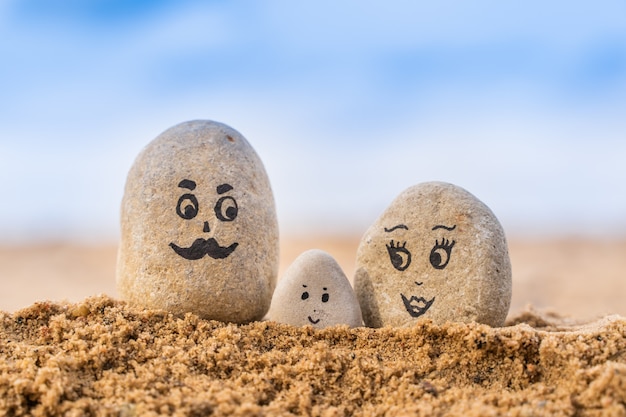 Grupo de piedras con caras dibujadas en la arena. Padre, madre e hijo. Concepto de familia feliz.